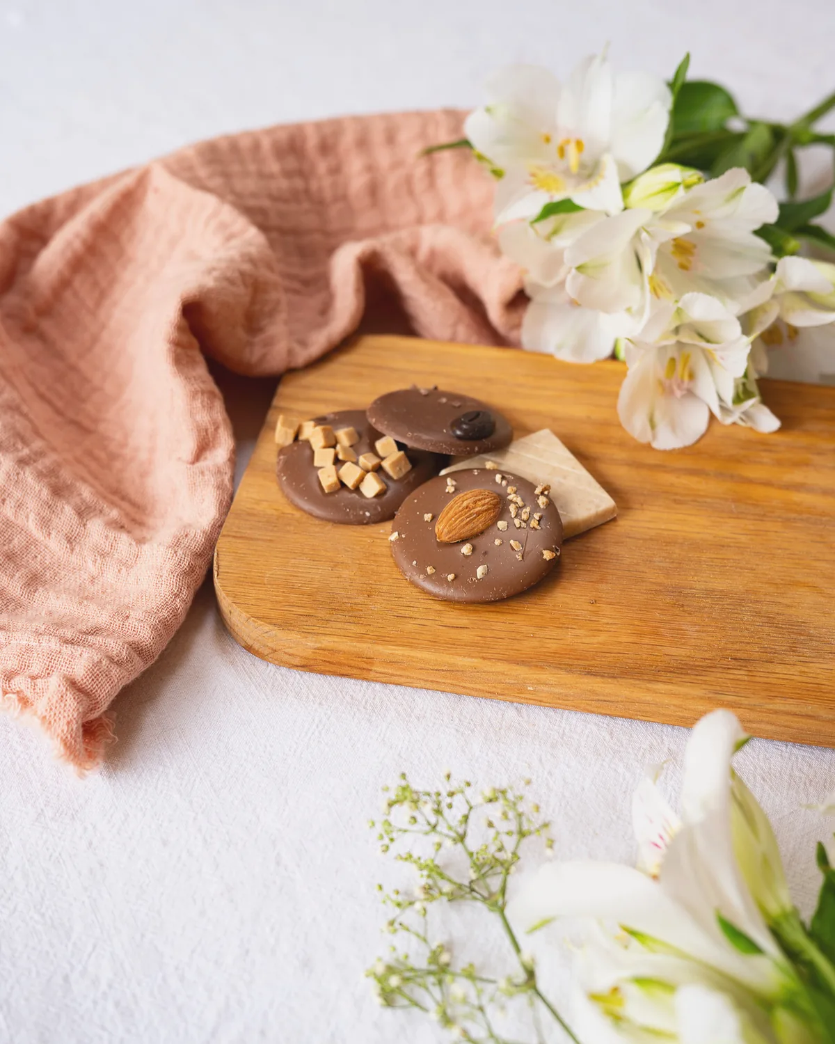 Schokoladenspezialitäten auf einem Holzbrett mit Blüten und Leinentuch